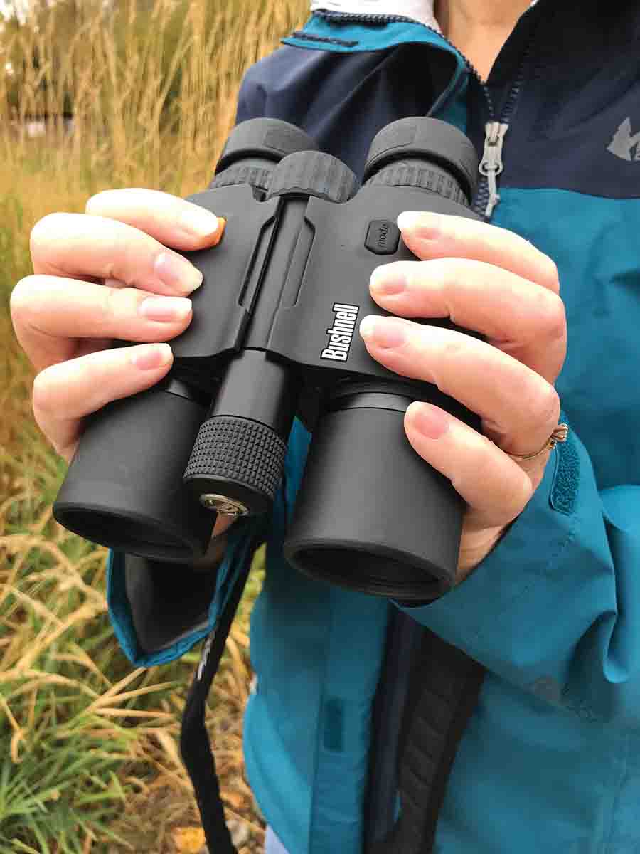 The Bushnell Fusion 10x42mm 1 Mile ARC rangefinding binocular has its orange range/power button placed right where the index finger of the right hand normally grasps a binocular. The battery compartment sticks out between the binocular’s barrels.